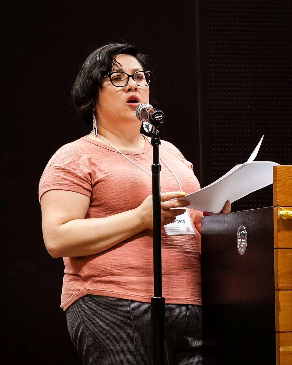 A woman speaking at a microphone while holding papers at a podium.